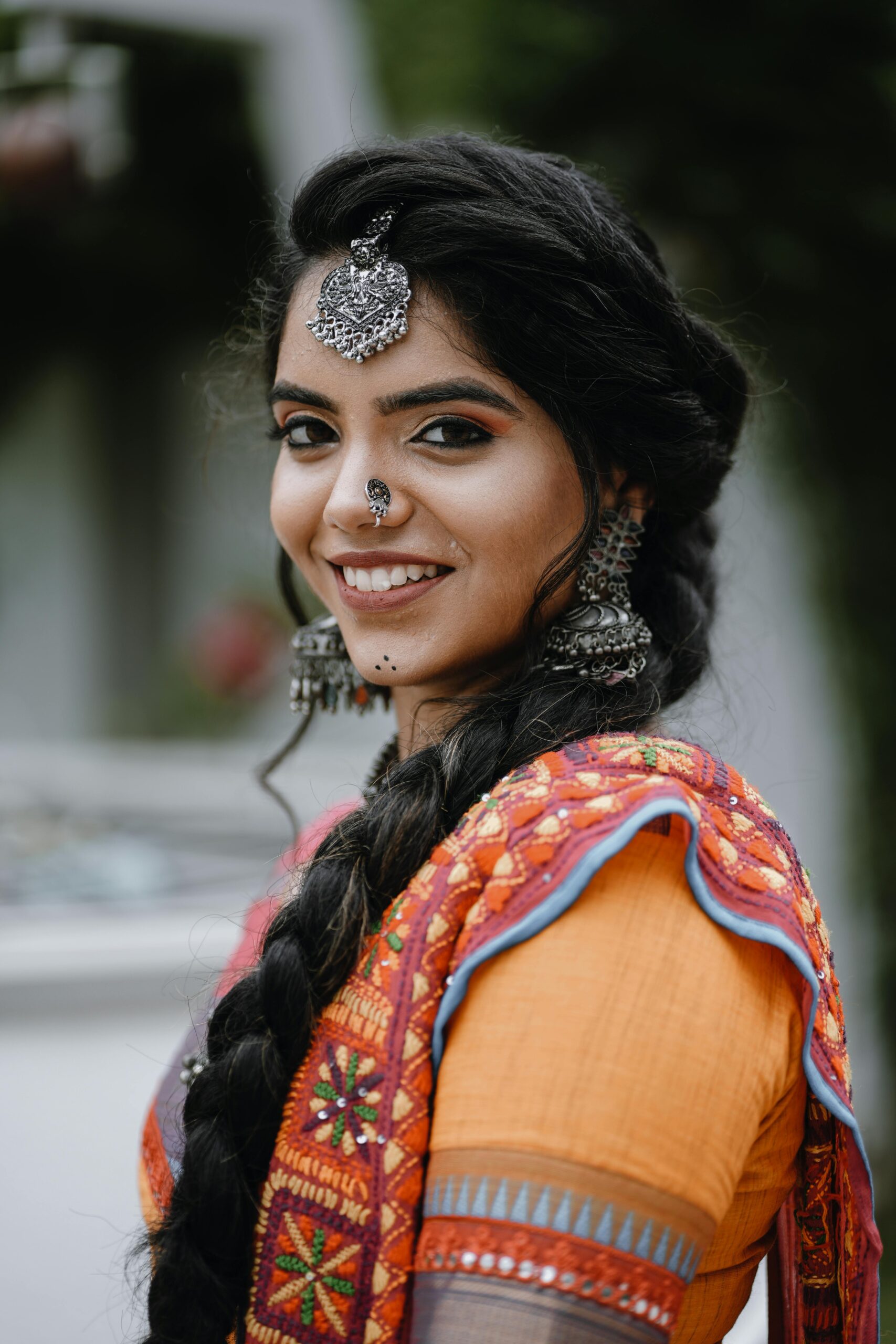 Portrait of a young woman in vibrant traditional Indian attire, smiling outdoors.